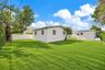 Single-story residence featuring a light-toned exterior, concrete driveway with decorative stone inserts, manicured lawn, and gated perimeter fencing