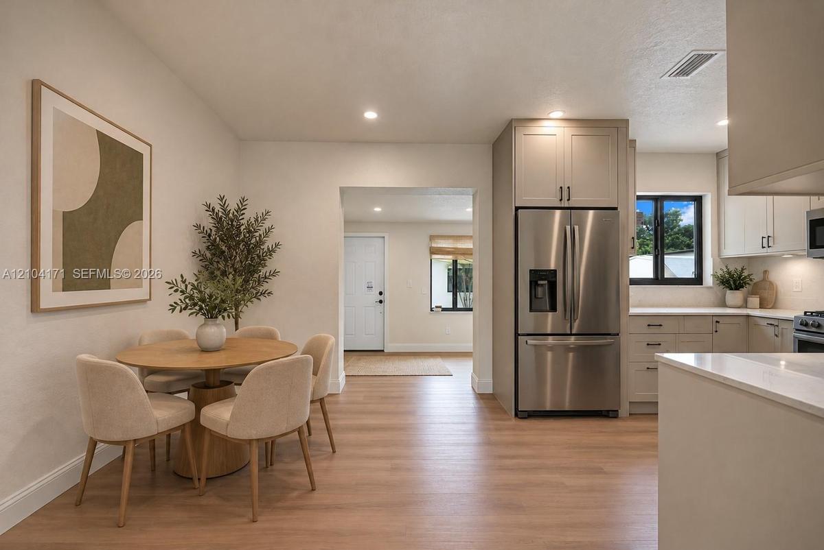 Kitchen featuring light-toned cabinetry, stainless steel refrigerator, stone countertops, and wood-finish flooring