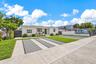 Single-story exterior with light-toned stucco finish, concrete driveway featuring permeable geometric pavers, manicured lawn, and opaque privacy fenci
