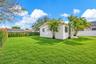 Expansive backyard featuring a manicured lawn, perimeter fencing, and mature palm trees