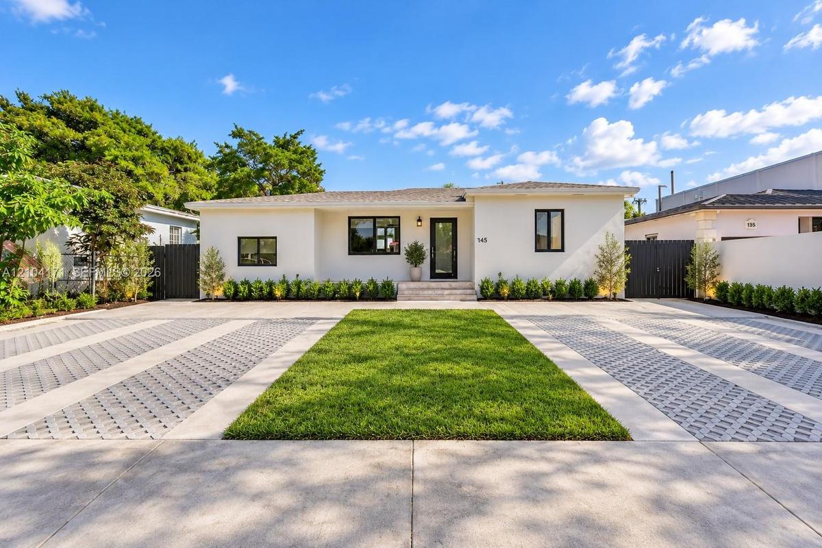 Single-story residence featuring a smooth stucco facade, contrast-trimmed windows, a central entryway with stone steps, and an expansive paved motor c
