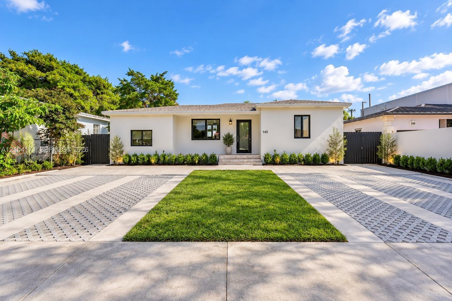 Single-story residence featuring a smooth stucco facade, contrast-trimmed windows, a central entryway with stone steps, and an expansive paved motor c