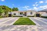 Single-story residence featuring a smooth stucco facade, contrast-trimmed windows, a central entryway with stone steps, and an expansive paved motor c