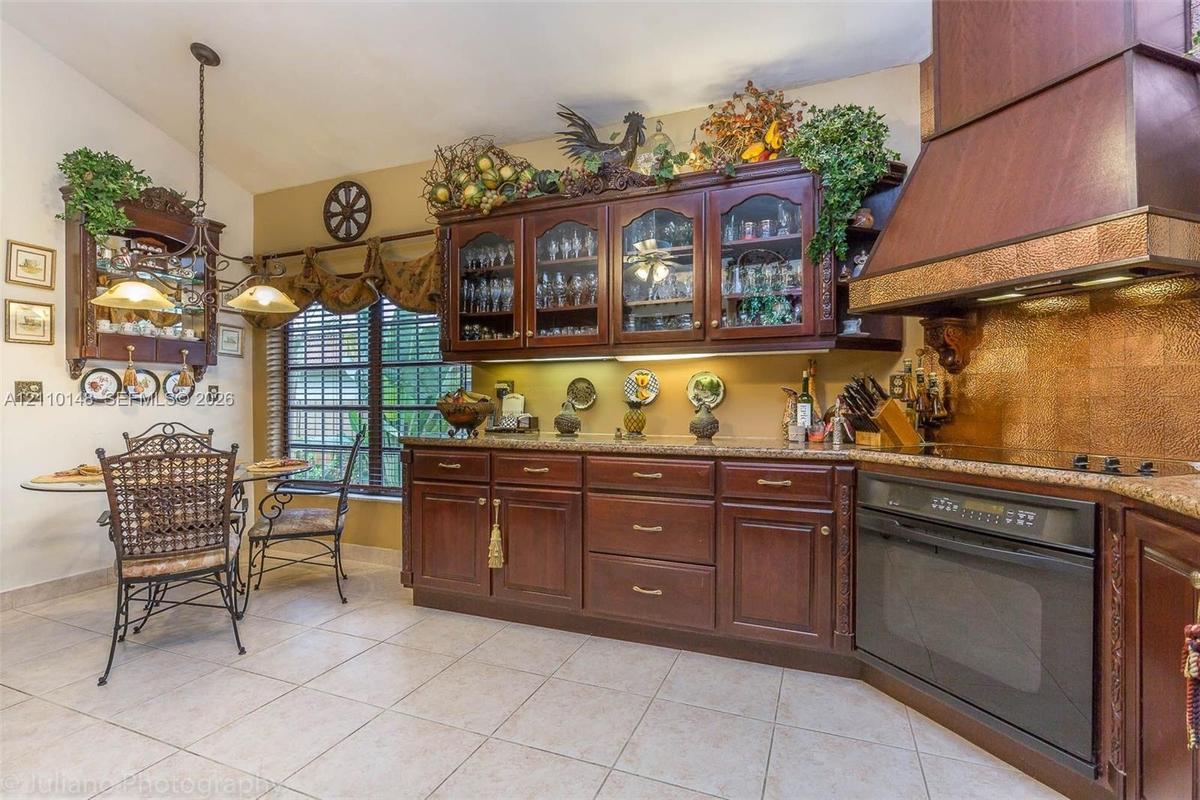 Kitchen featuring custom wood cabinetry with glass-front display uppers, stone-surface countertops, decorative metallic backsplash, a large wood-finis