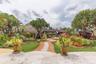 Landscaped backyard featuring a stone-paved patio, a thatched-roof gazebo, mature tropical vegetation, and a brick walkway