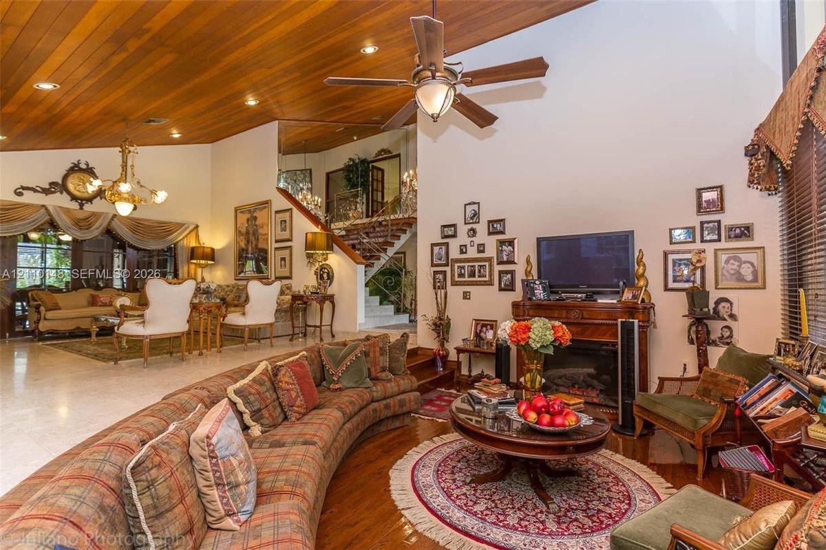 Vaulted ceiling with wood-plank finish, recessed lighting, ceiling fan, fireplace with ornate mantle, and staircase with metal railing