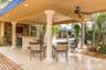 Covered outdoor patio featuring stone flooring, integrated bar with cabinetry, structural decorative columns, recessed lighting, and dual ceiling fans