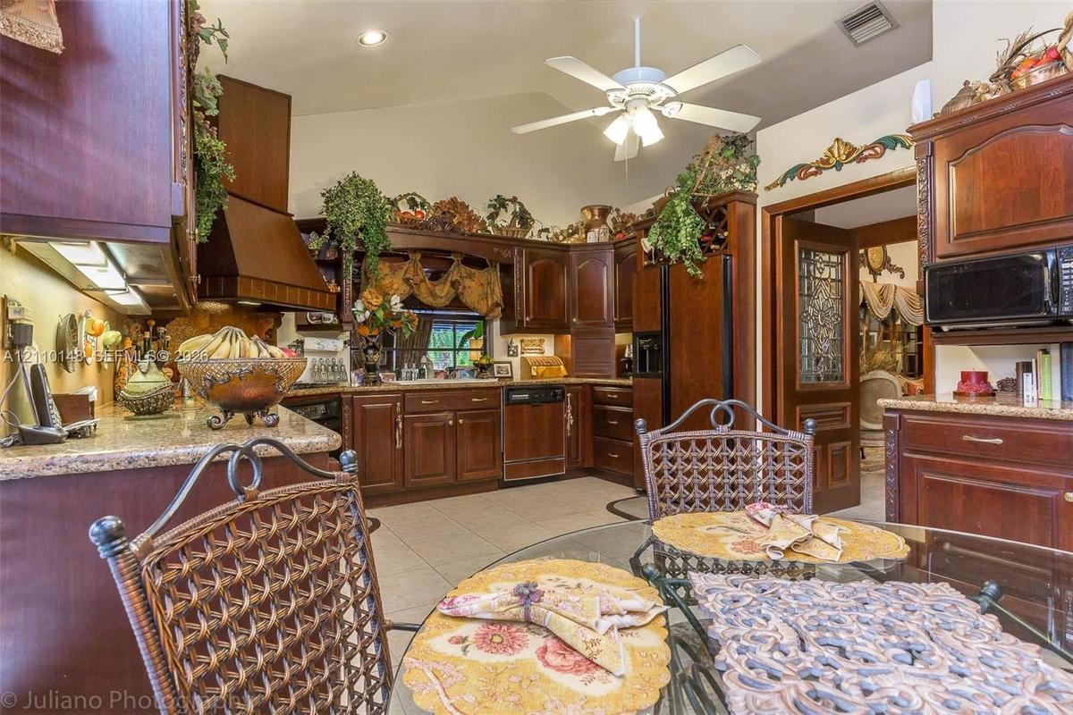 Kitchen featuring stained wood cabinetry, stone countertops, tiled flooring, vaulted ceilings, and a decorative door with glass detailing