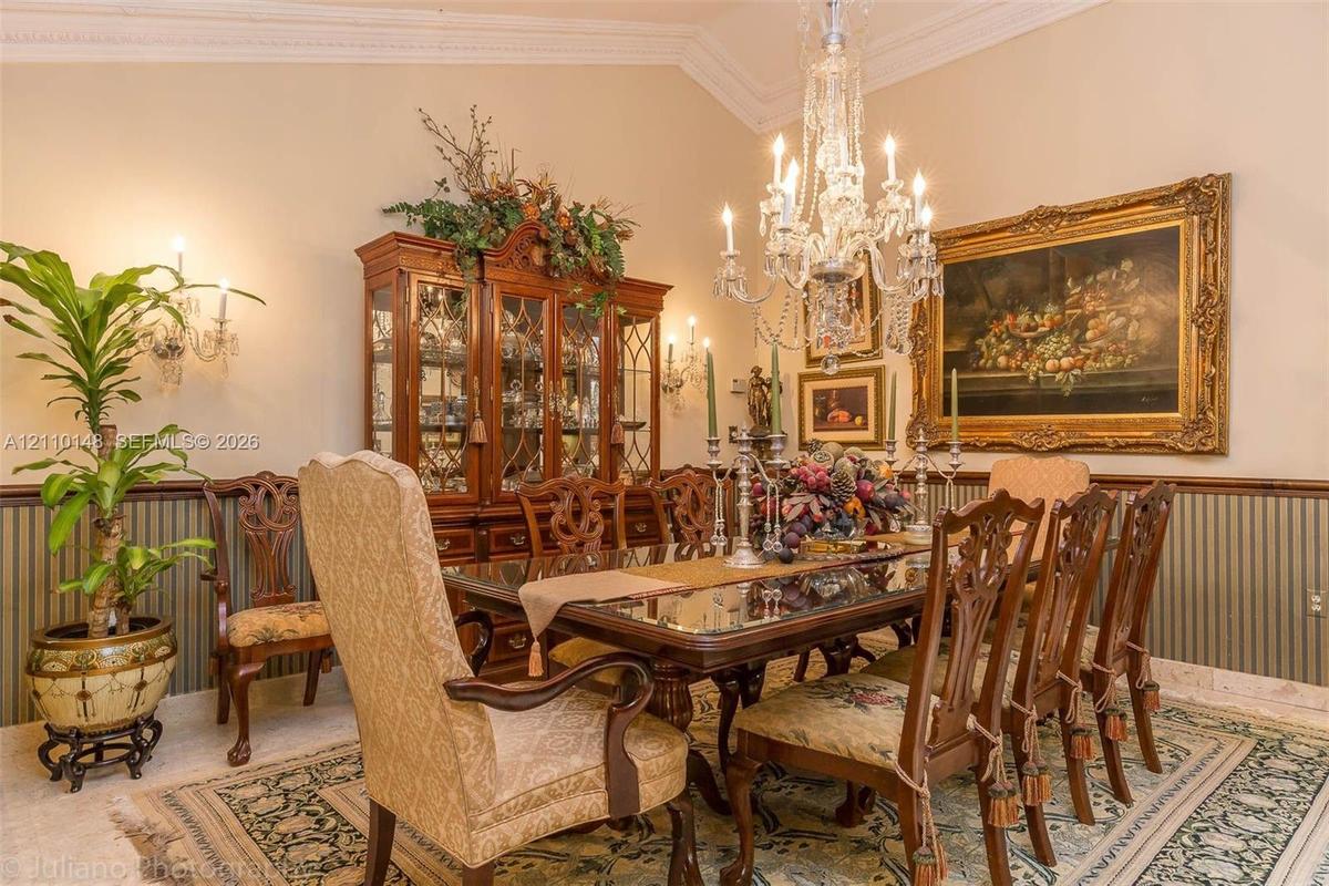 Formal dining space featuring intricate crown molding, decorative chair rail, wall-mounted light sconces, and a multifaceted crystal chandelier
