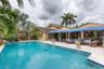 In-ground swimming pool with stone-tiled decking, retractable blue awning, and detached covered patio featuring a built-in bar