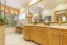 Dual-vanity cabinetry with intricate wood carvings and stone countertops, large wall-mounted mirror with gold-tone detailing, stone wall and floor til