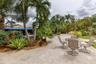 Expansive stone-paved patio featuring established palm trees, landscaped garden beds, and manicured lawn areas