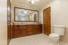 Dual-sink vanity with wood-finish cabinetry, solid surface countertop, expansive wall-mounted mirror, and tile-finished walls