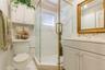 Bathroom featuring a corner glass-enclosed shower with gold-tone hardware, white cabinetry, a built-in wall cabinet, and decorative tile border trim