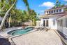 Free-form swimming pool with tile surround, expansive paver patio, white stucco exterior, tile roofing, and glass block accent walls