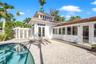 Exterior featuring white stucco siding, a curved in-ground pool, expansive stone-paver patio, glass-block privacy wall, and multi-pane transom windows