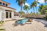 Backyard featuring a paver patio, in-ground pool with a decorative stone water feature, mature palm trees, and wood-style privacy fencing