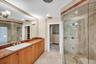 Bathroom featuring a stone-topped vanity with an integrated basin, expansive wall-mounted mirror, glass-enclosed shower with stone tile surround, and 