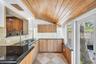Vaulted tongue-and-groove wood ceiling, polished stone countertops, light wood cabinetry, glass block accent wall, and stone-tile flooring