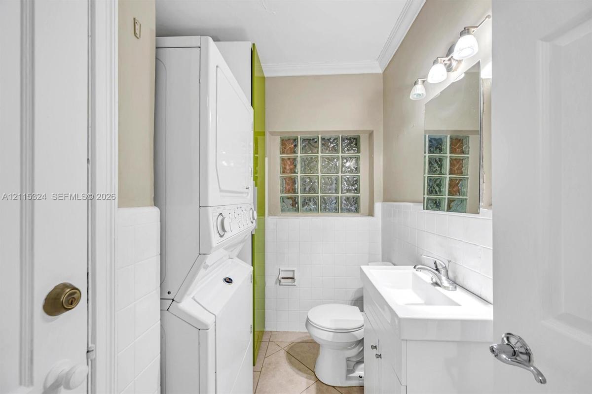 Combination laundry area and bathroom featuring a stacked washer and dryer, square glass block window, white vanity with integrated sink, and polished