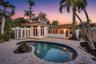Exterior space featuring a kidney-shaped swimming pool, paved stone patio, raised architectural cupola, glass block screen, and mature palm trees