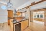 Kitchen featuring custom wood cabinetry, stone-topped island with integrated beverage refrigerator, stainless steel range hood, stone tile backsplash,