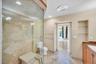 Walk-in shower with natural stone tile surround and built-in bench, glass enclosure, stone tile flooring, built-in wall shelving, and cabinetry with s