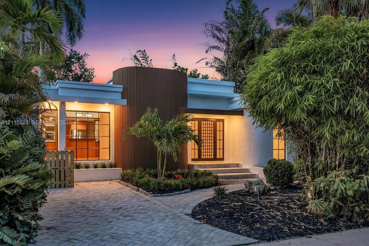 Mid-century modern exterior featuring vertical wood-slat siding, a geometric grid-pattern front door, large-format grid windows, and a paved brick dri