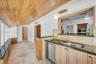 Vaulted natural wood plank ceiling, tile flooring, stone-finish countertops, stainless steel dual-basin sink, and built-in cabinetry