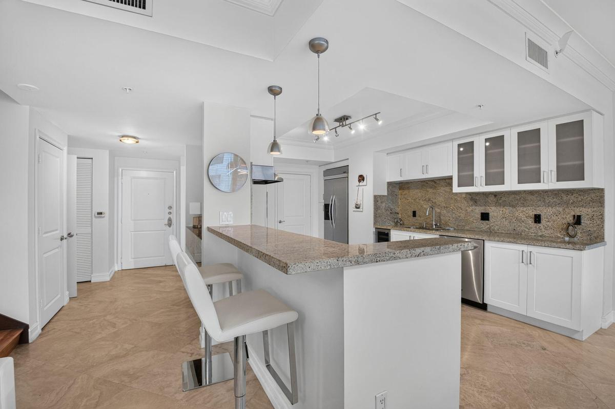 Kitchen featuring granite countertops, stainless steel appliances, white cabinetry with frosted glass, and pendant lighting.