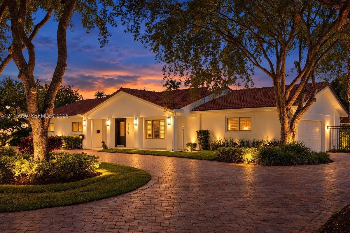 Single-story residence featuring a tile roof, light-toned exterior finish, and a brick-paver circular driveway surrounded by mature landscaping
