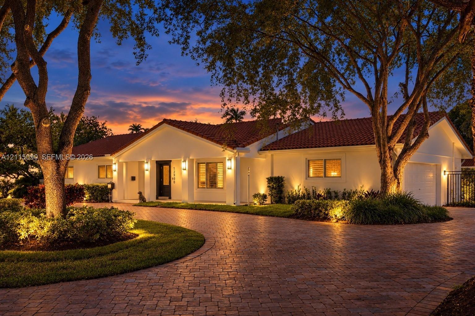 Single-story residence featuring a tile roof, light-toned exterior finish, and a brick-paver circular driveway surrounded by mature landscaping