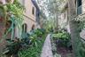 Stucco exterior featuring arched breezeways and second-story balcony railings, accented by a herringbone-patterned paver walkway and mature landscapin