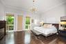 Spacious room featuring wood-finish tile flooring, crown molding, a central multi-arm chandelier, and two glass-panel doors leading to an exterior bal