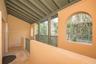 Covered balcony featuring natural stone flooring, arched openings, exposed ceiling beams, and integrated railing