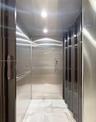 Private elevator featuring polished stainless steel wall panels, recessed ceiling lighting, a horizontal handrail, and large-format tile flooring with