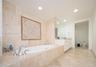 Stone-tiled soaking tub surround with decorative mosaic inlay, recessed lighting, expansive wall-mounted mirror, and stone flooring