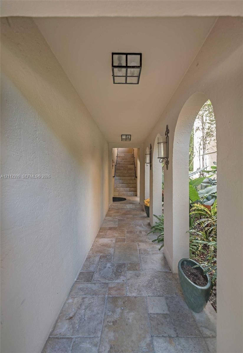 Covered walkway featuring a series of architectural arches, stone tile flooring, wall-mounted lantern-style lighting, and flush-mount overhead lightin