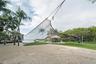 Sandy outdoor recreation area featuring a volleyball net, grass lawn, thatch-roofed gazebo, and mature palm trees