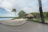 Waterfront lot featuring a sandy beach, a thatched-roof tiki hut, mature palm trees, and lush perimeter landscaping