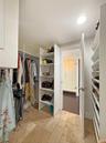 Walk-in closet featuring custom white built-in shelving, hanging rods, and natural stone tile flooring