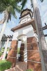 Architectural tower featuring a stucco exterior, decorative stone-finish base, arched entryway, and attached lantern-style lighting fixtures, set atop