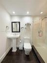 Pedestal sink with chrome widespread faucet, walk-in shower featuring a glass enclosure and wall-mounted hand shower, dark tile flooring, and integrat