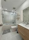 Bathroom featuring a wood-finish floating vanity with a white integrated sink, glass-enclosed shower and tub combination with a rain-style showerhead,
