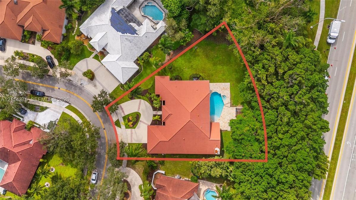 Aerial perspective of a property featuring a tile roof, a paved circular driveway, a rear swimming pool, and mature landscaping