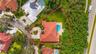 Aerial perspective of a property featuring a tile roof, a paved circular driveway, a rear swimming pool, and mature landscaping