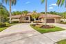 Stucco exterior featuring a terracotta-tile roof, expansive concrete driveway with brick inlay, and mature palm landscaping