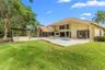 Rear exterior featuring a swimming pool, stone-paver patio, built-in outdoor bar, and manicured lawn with mature trees