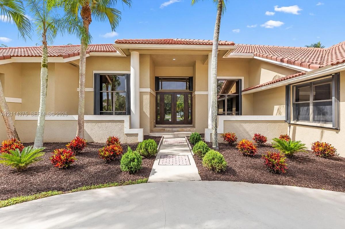 Stucco exterior featuring a terracotta tile roof, central recessed entryway with dual glass-paneled doors, decorative column accents, and a paved walk