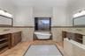 Freestanding clawfoot tub, dual wooden vanity cabinetry with stone countertops, decorative tile floor inlay, and wall-mounted vanity lighting